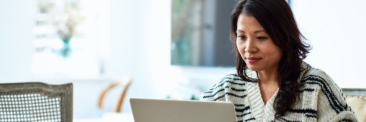 A woman sitting at her dining table and typing on her laptop.