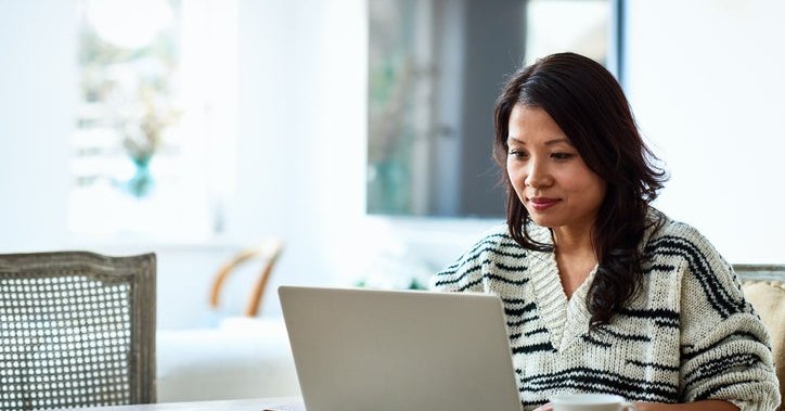 A woman sitting at her dining table and typing on her laptop.