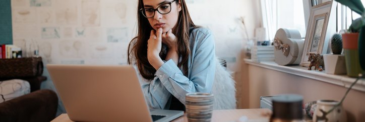 A worried-looking woman looking something up on her laptop while sitting at her kitchen table.