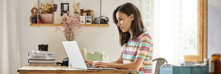 A woman looking something up on her laptop while sitting at a table in her home.
