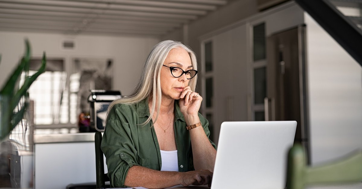 A woman searching on her laptop while sitting at her kitchen table.