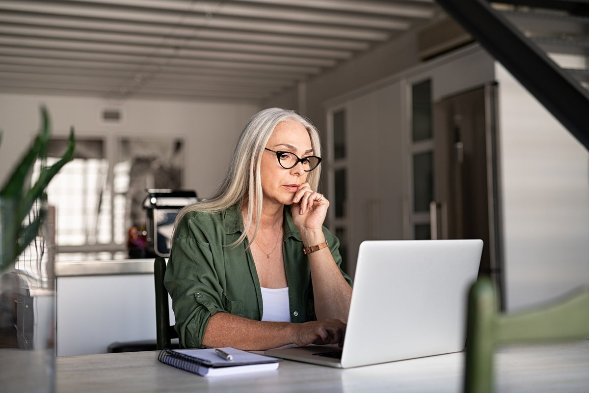 A woman searching on her laptop while sitting at her kitchen table.