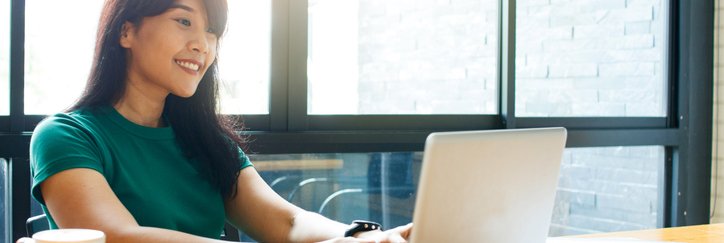 A smiling woman typing on her laptop while sitting in a cafe.