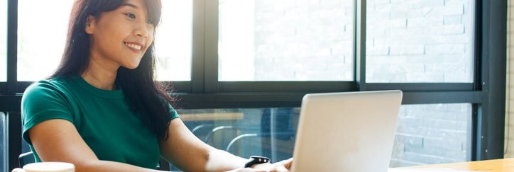 A smiling woman typing on her laptop while sitting in a cafe.