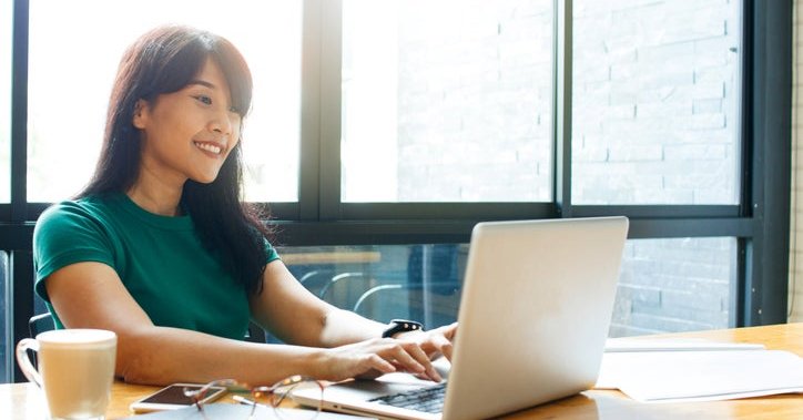 A smiling woman typing on her laptop while sitting in a cafe.