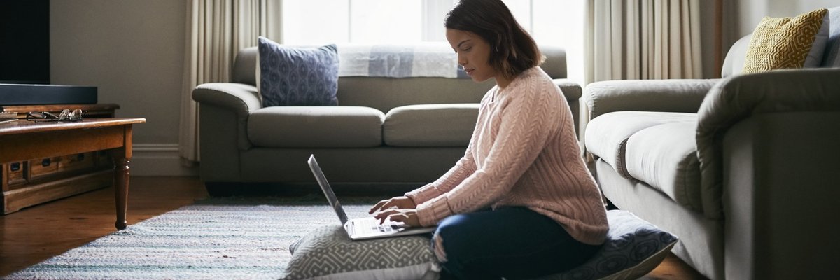 A young woman working from home on her laptop while sitting on the living room floor.