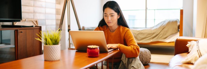 A woman sitting on her living room floor and looking up something on her laptop on the coffee table.