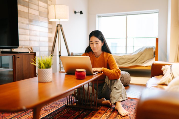 A woman sitting on her living room floor and looking up something on her laptop on the coffee table.