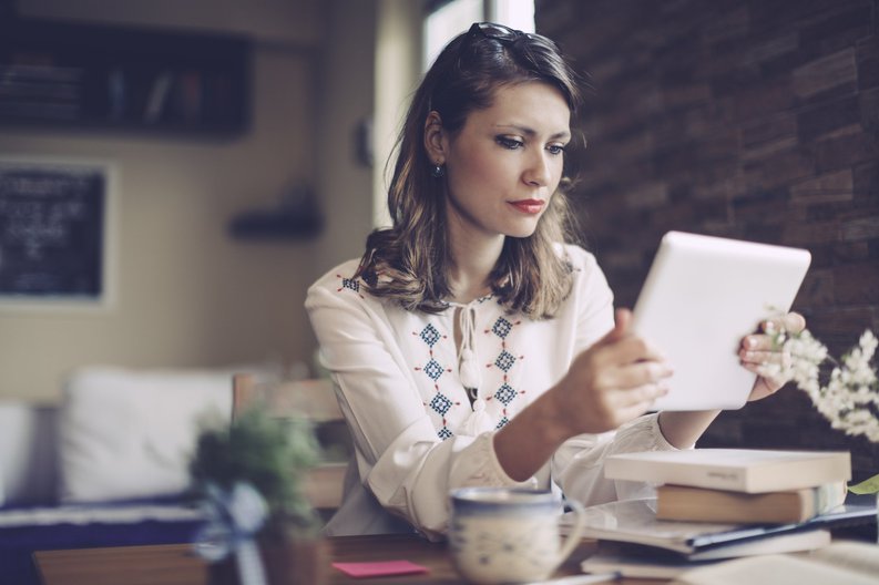 A woman looking at a tablet while sitting at a table in her living room.