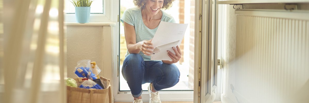 A woman smiling while opening mail in her sunny entryway.