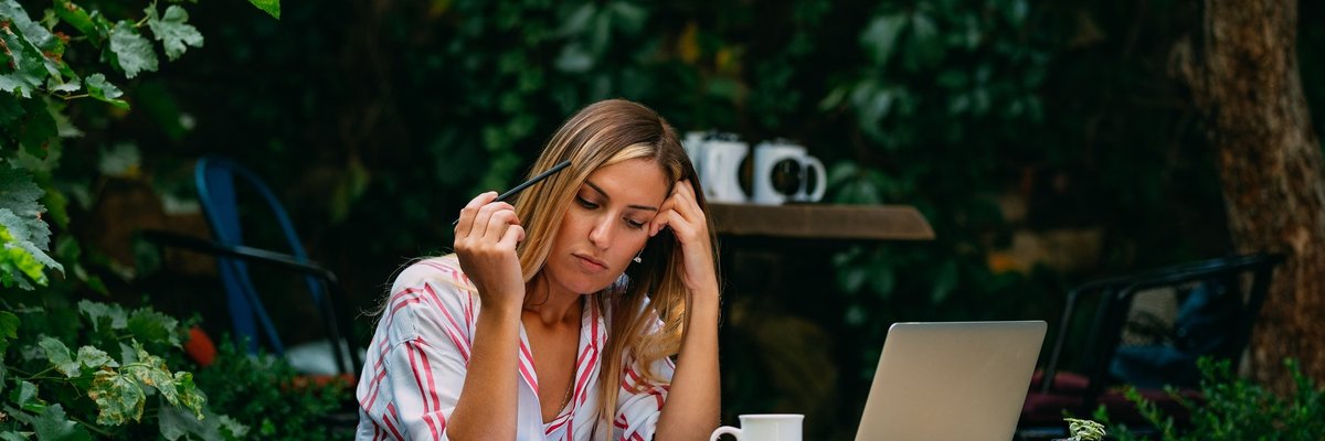 A woman sitting at an outdoor cafe with a laptop and notebook open.