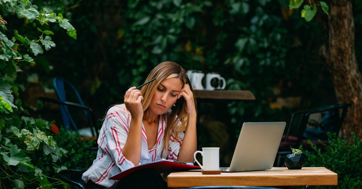 A woman sitting at an outdoor cafe with a laptop and notebook open.