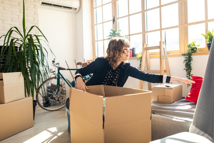 A young woman packing moving boxes in the living room of her sunny apartment.