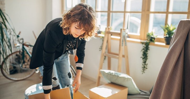 A woman packing moving boxes in a sunny apartment.