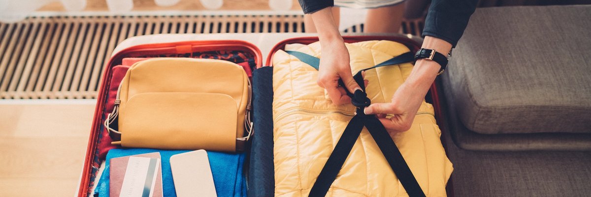 A woman packing a suitcase with her credit card, passport, and phone on top.
