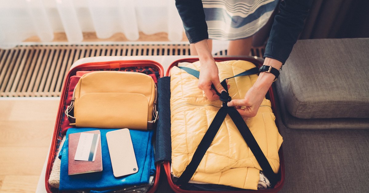 A woman packing a suitcase with her credit card, passport, and phone on top.