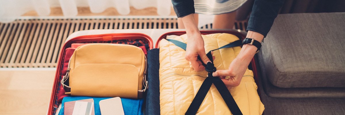 A woman packing a suitcase with her credit card, passport, and phone on top.