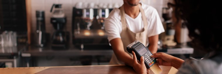 A woman swiping her credit card in the payment machine being held over the counter by a cafe cashier.