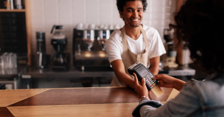 A woman swiping her credit card in the payment machine being held over the counter by a cafe cashier.