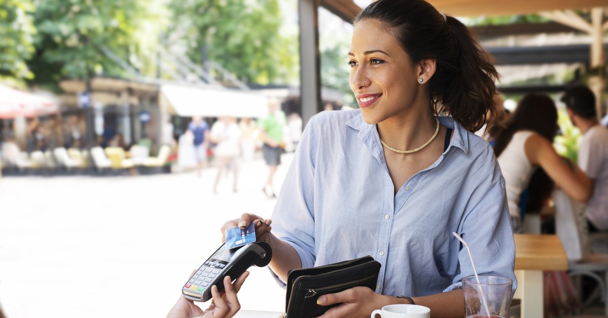 A woman sitting at a patio table and paying a waitress with her credit card.
