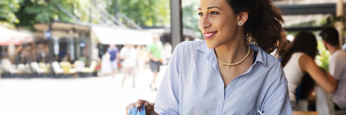 A woman sitting at a patio table and paying a waitress with her credit card.