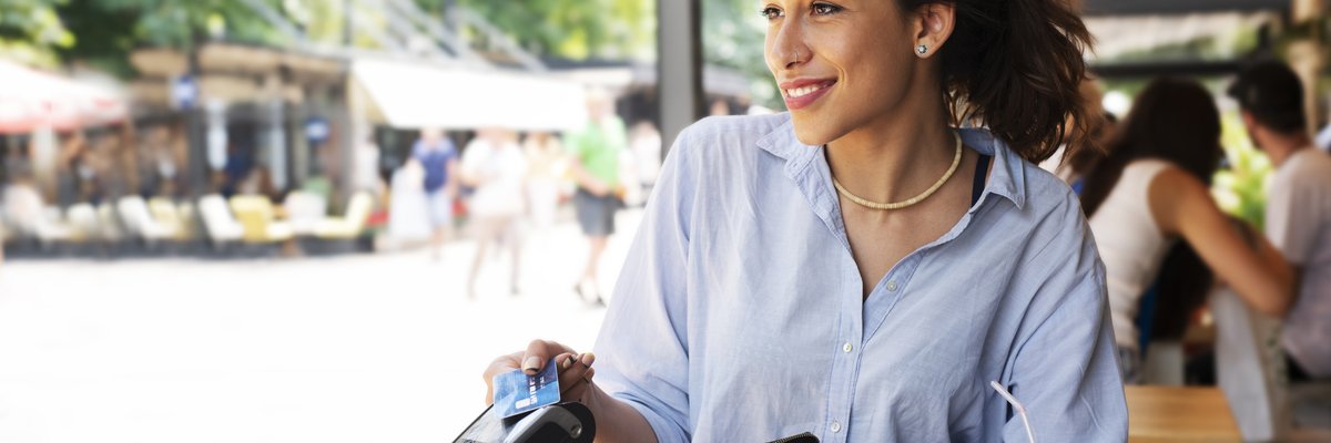 A woman sitting at a patio table and paying a waitress with her credit card.