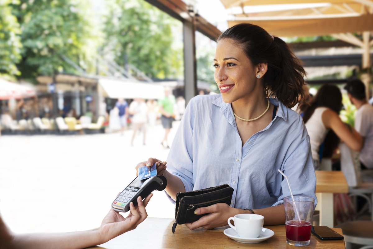 A woman sitting at a patio table and paying a waitress with her credit card.