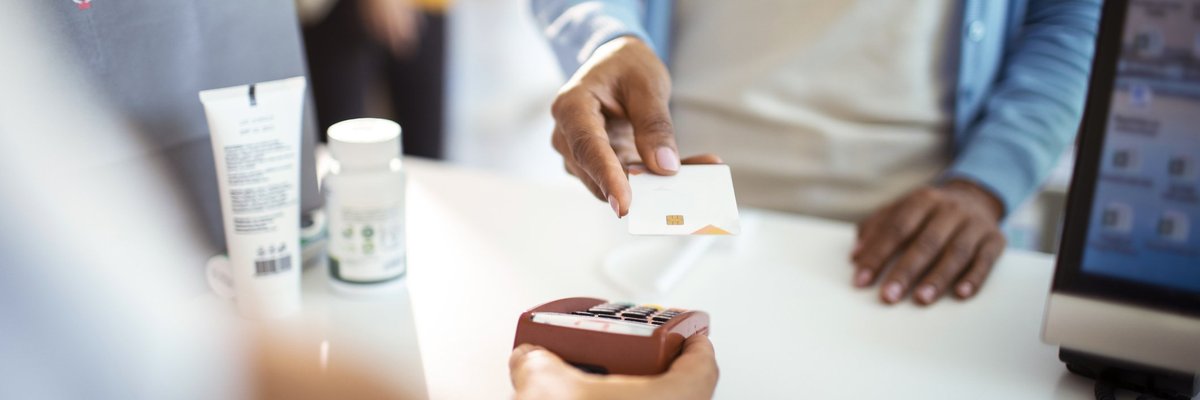 A woman holding her credit card up to the payment reader at the pharmacy.