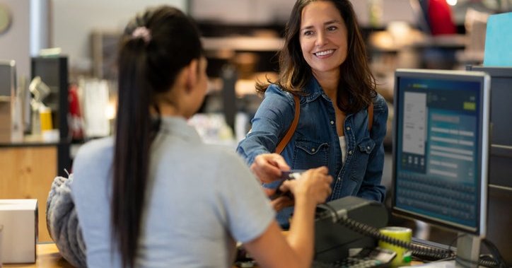 A woman handing her credit card to the employee at a cashier stand in a department store.