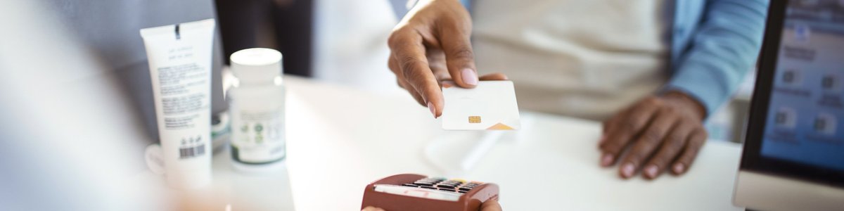 A woman holding her credit card up to the payment reader at the pharmacy.