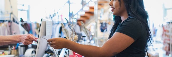 A woman handing her credit card to the cashier behind the counter in a clothing store.
