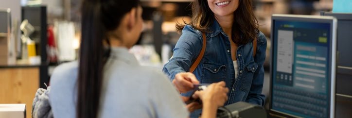 A woman handing her credit card to the employee at a cashier stand in a department store.