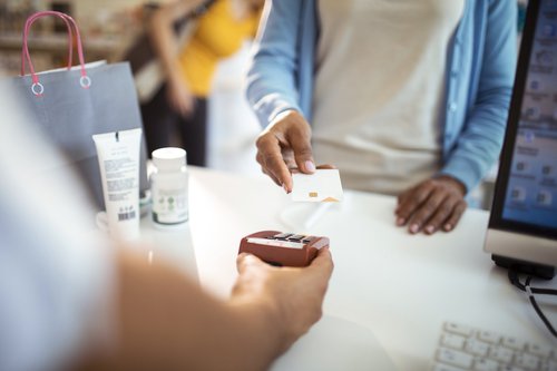 A woman holding her credit card up to the payment reader at the pharmacy.