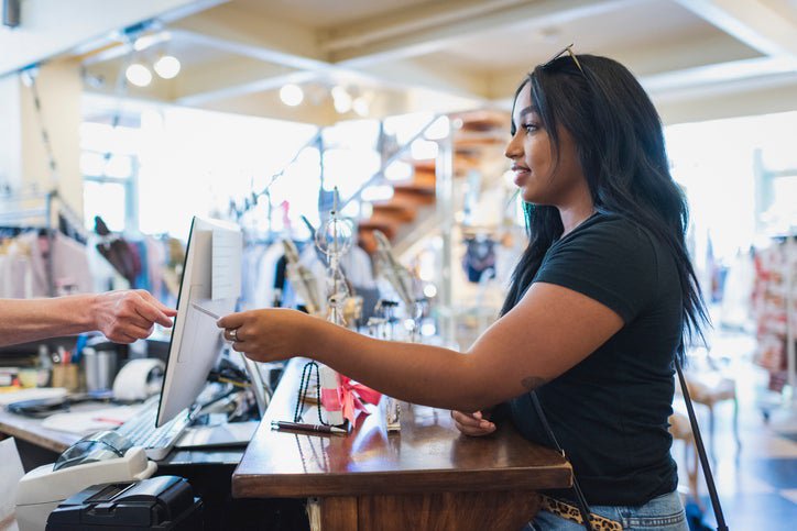 A woman hands her credit card to a cashier behind the counter in a clothing store.