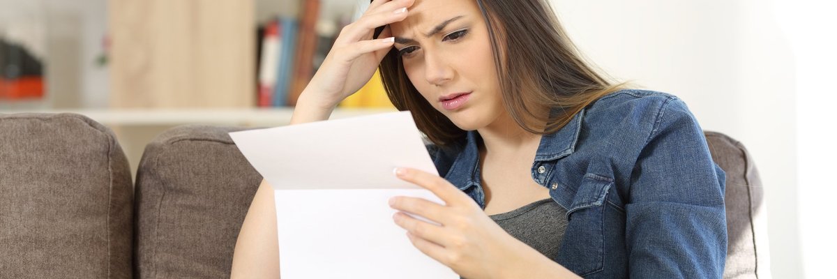 woman sitting on couch reading document while holding her head
