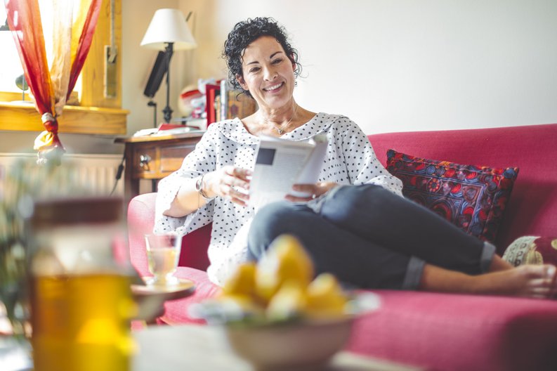 A woman reading a magazine on a couch in a colorfully decorated living room.