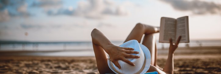 A woman lying on the beach reading a book.