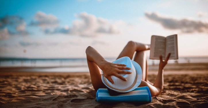 A woman lying on the beach reading a book.