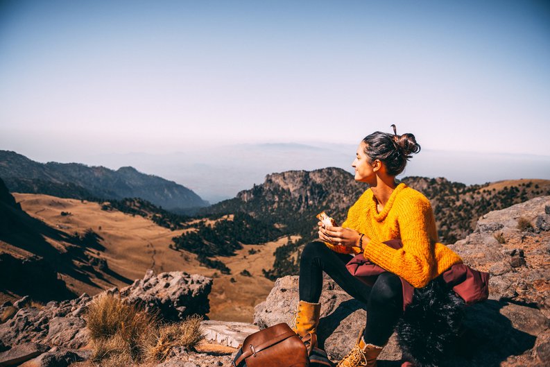 A female hiker taking a break for lunch on top of a hill and admiring the view.
