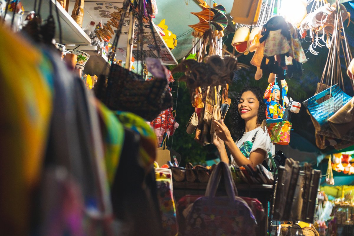 A young woman happily looking at handmade items in the booth at a craft market.