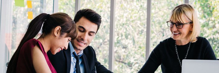 A smiling woman signing documents while sitting at a table with her husband and their realtor.