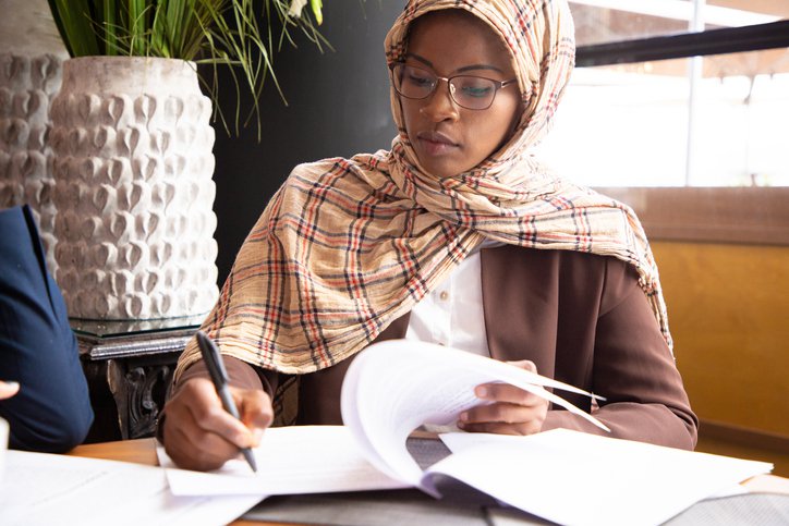 A woman sitting at a table in an office meeting room and signing paperwork.