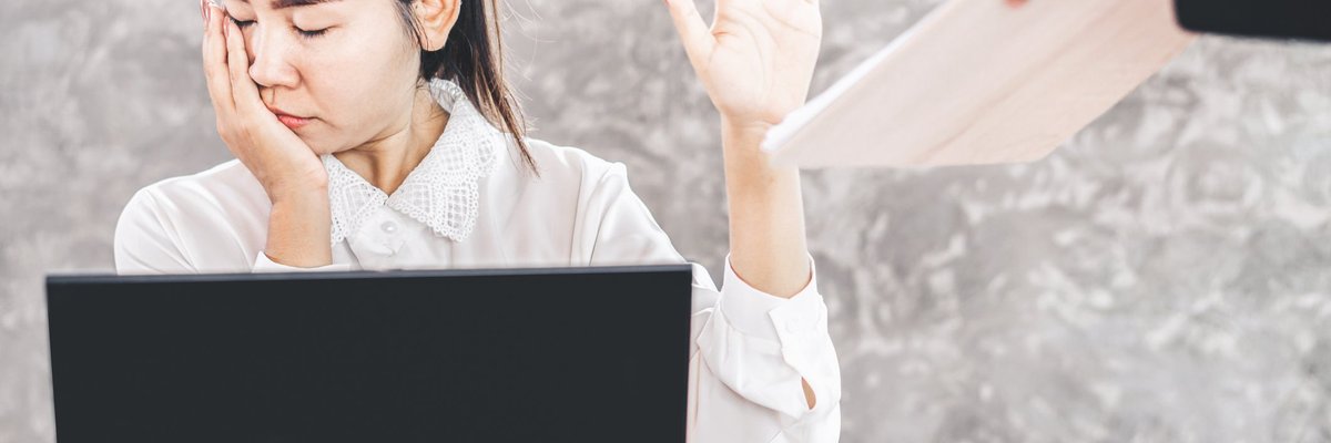 woman sitting at desk looking away and holding up her hand as a coworker tries to hand her a document.