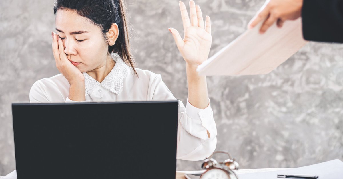 woman sitting at desk looking away and holding up her hand as a coworker tries to hand her a document.