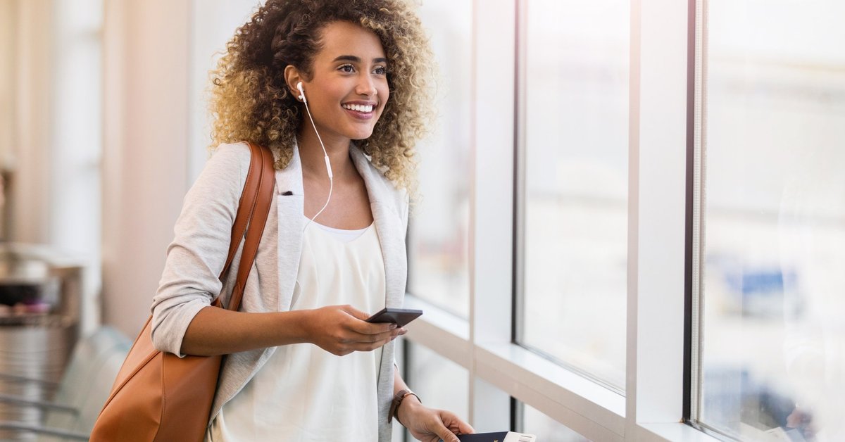 A woman smiling in an airport with her suitcase and passport.
