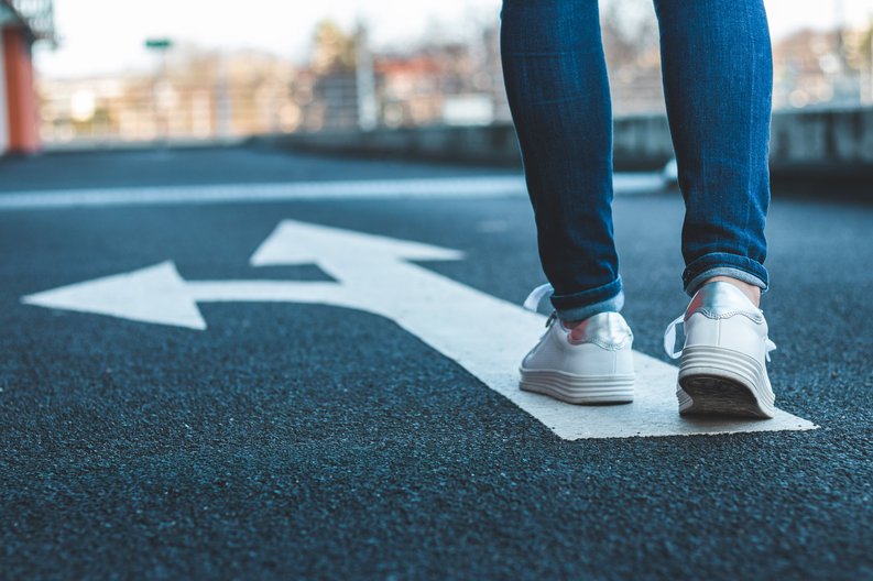A woman's feet standing on an arrow painted in the street that's pointing in two directions.