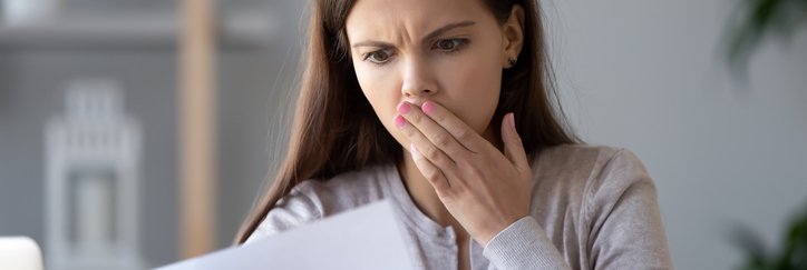 A woman holds her hand over her mouth in surprise at a bill.