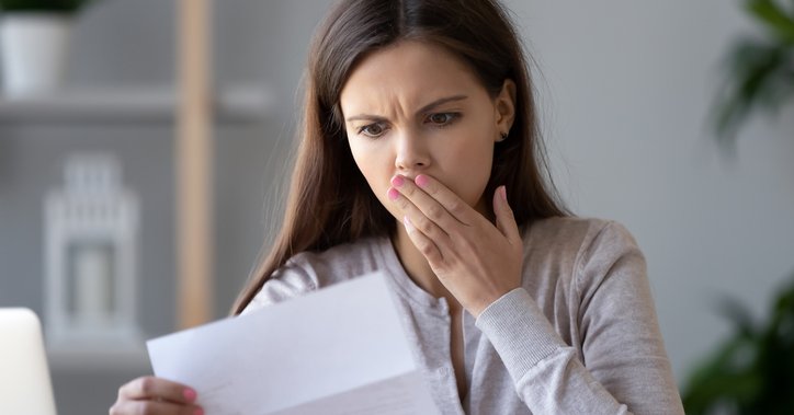 A woman holds her hand over her mouth in surprise at a bill.