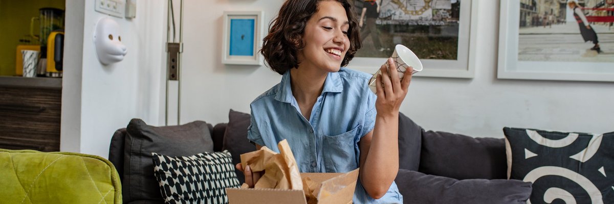 Smiling woman on couch looks at a mug she's getting out of a box
