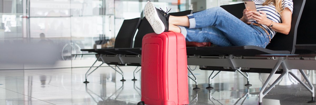 A woman wearing a mask sits and waits at an empty departure gate.